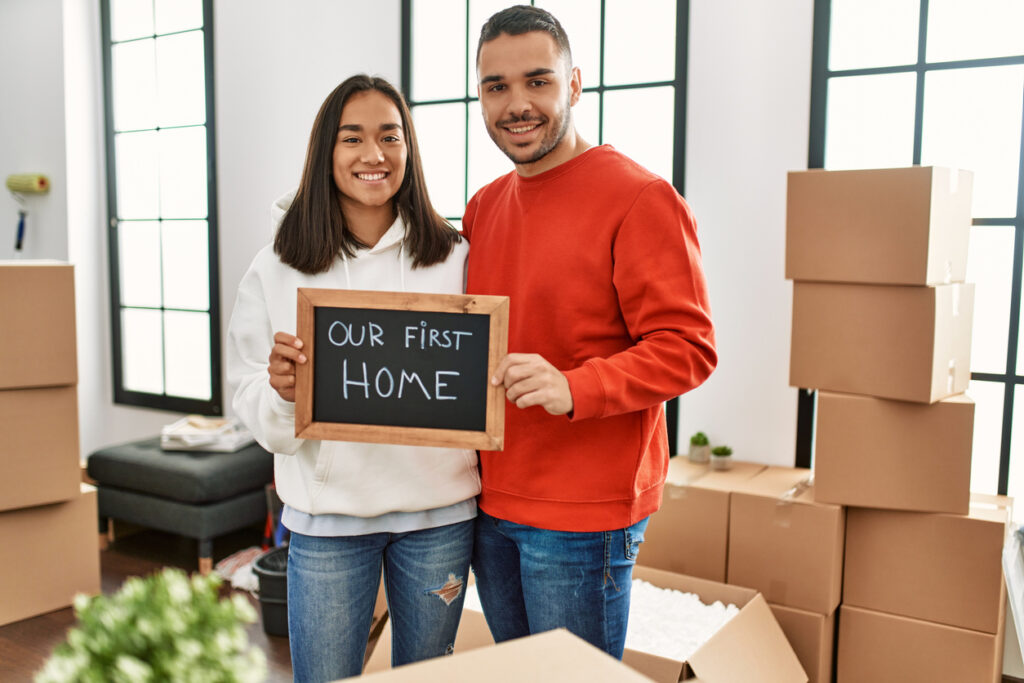 Young couple smiling happy holding blackboard with our first home message.